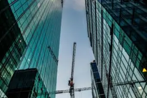 Looking up at modern skyscrapers with construction cranes in a bustling cityscape.